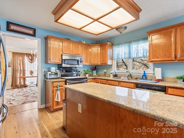 kitchen featuring appliances with stainless steel finishes, sink, a chandelier, light stone countertops, and light wood-type flooring