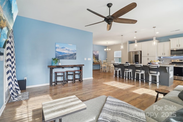 living room featuring ceiling fan with notable chandelier and light hardwood / wood-style floors