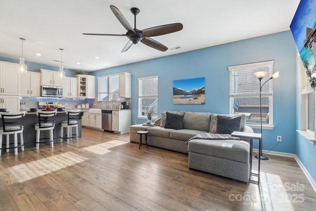 living room featuring ceiling fan, sink, and light wood-type flooring