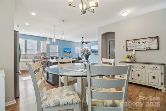 dining area featuring dark wood-type flooring, plenty of natural light, sink, and ceiling fan with notable chandelier