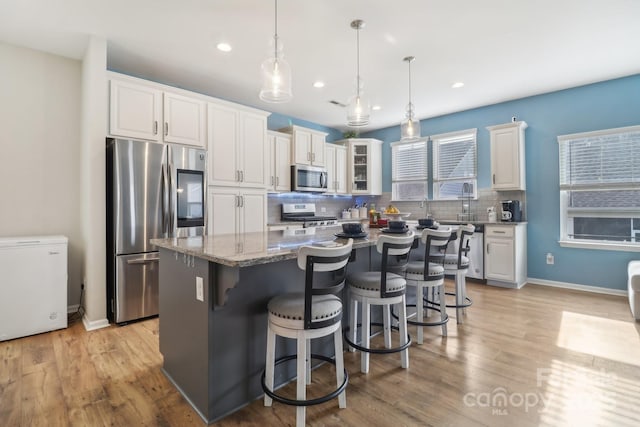 kitchen featuring white cabinetry, light stone counters, appliances with stainless steel finishes, a kitchen island, and pendant lighting