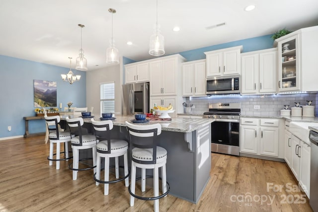 kitchen with pendant lighting, white cabinetry, a center island, stainless steel appliances, and light stone countertops