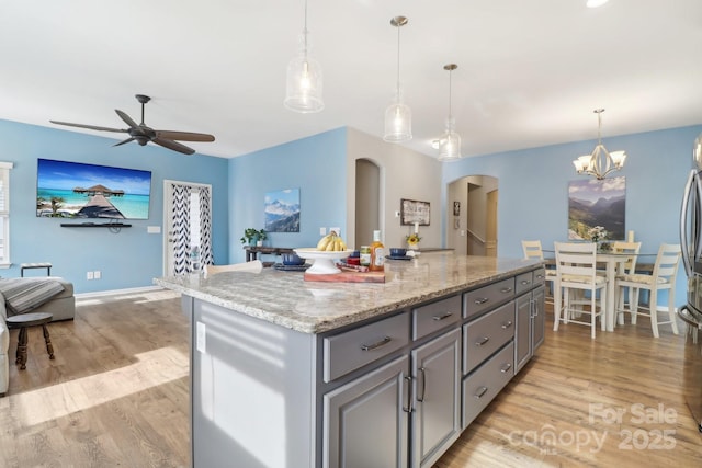 kitchen featuring gray cabinetry, hanging light fixtures, light stone countertops, and a center island