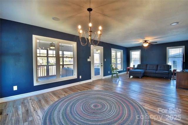 unfurnished living room featuring ceiling fan with notable chandelier, wood finished floors, and baseboards