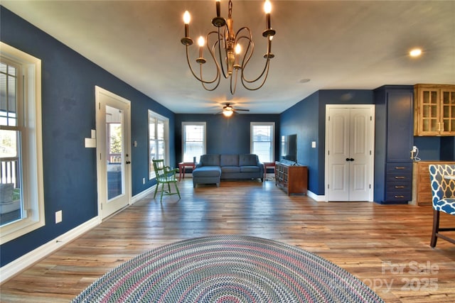 living room with ceiling fan with notable chandelier, wood finished floors, and baseboards