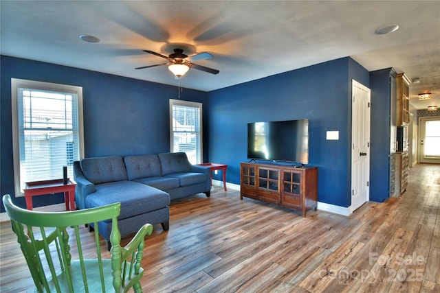 living area featuring wood finished floors, baseboards, and ceiling fan