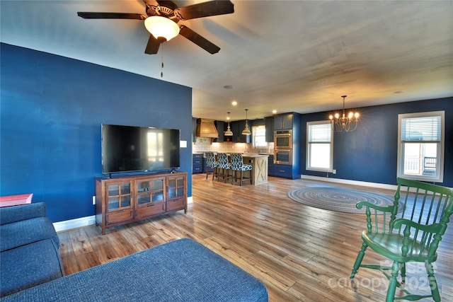 living area with baseboards, light wood-style floors, and ceiling fan with notable chandelier