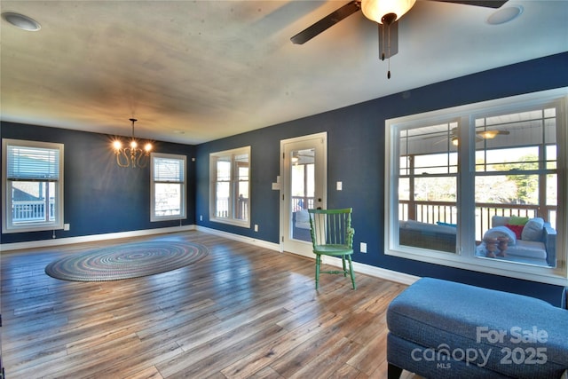 interior space with a wealth of natural light, baseboards, wood finished floors, and ceiling fan with notable chandelier