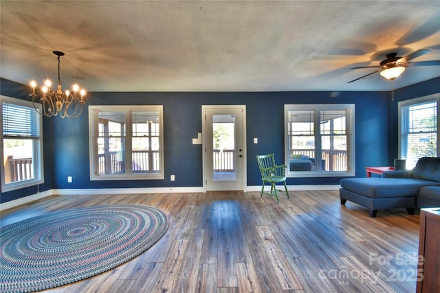 unfurnished living room with ceiling fan with notable chandelier, baseboards, and wood-type flooring