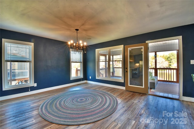 unfurnished room with hardwood / wood-style floors, a notable chandelier, and baseboards