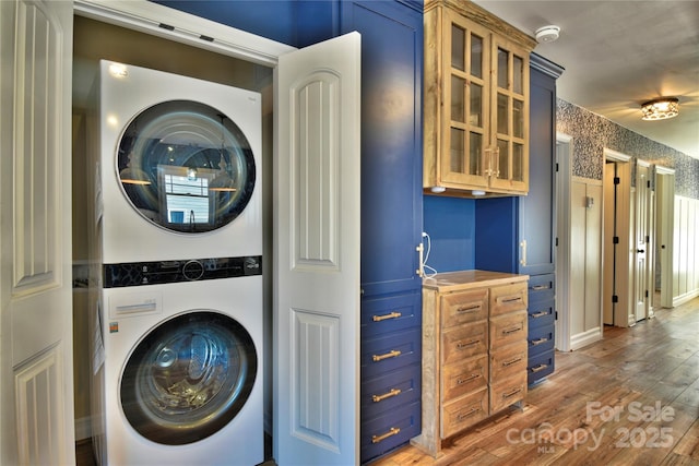 clothes washing area featuring stacked washer and dryer, laundry area, and hardwood / wood-style flooring