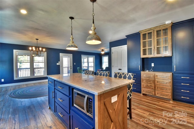 kitchen with hardwood / wood-style floors, a breakfast bar area, stainless steel microwave, decorative light fixtures, and a center island