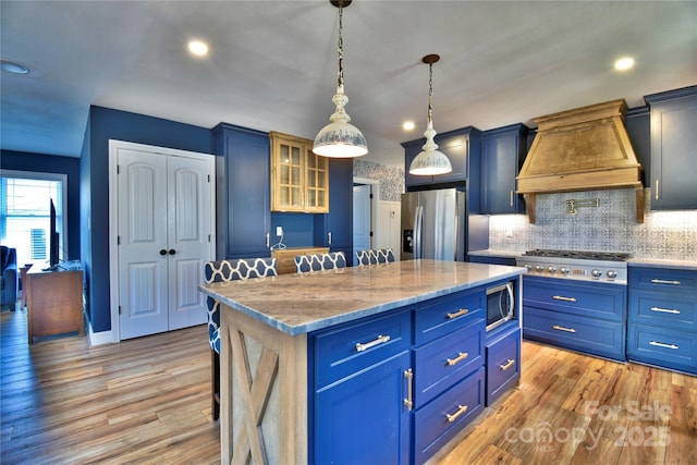 kitchen featuring light wood-style flooring, a center island, appliances with stainless steel finishes, glass insert cabinets, and custom exhaust hood