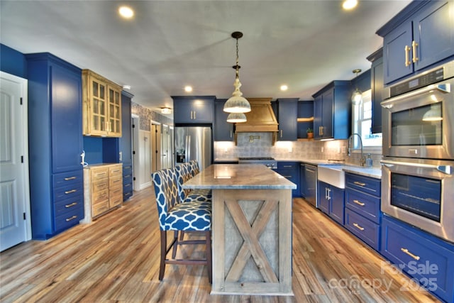 kitchen with a kitchen island, premium range hood, appliances with stainless steel finishes, wood finished floors, and blue cabinets