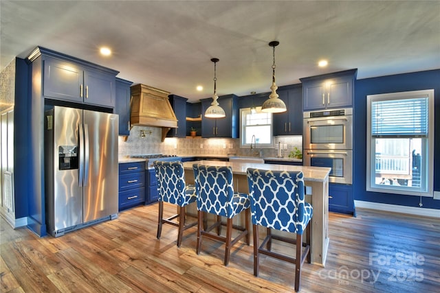 kitchen with blue cabinetry, appliances with stainless steel finishes, light wood-style flooring, and custom range hood