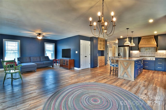 living area with ceiling fan with notable chandelier, wood finished floors, and baseboards