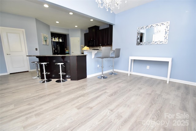 kitchen with black fridge with ice dispenser, a breakfast bar area, light hardwood / wood-style floors, and kitchen peninsula