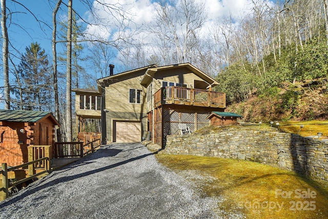 view of side of property with a deck, a storage shed, an attached garage, and gravel driveway