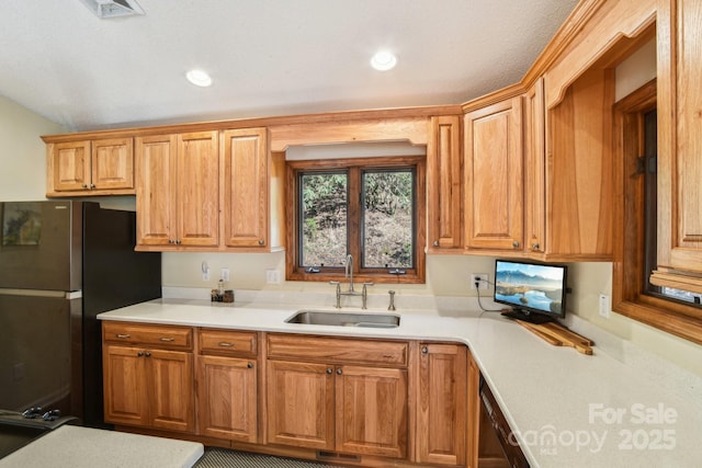 kitchen featuring brown cabinetry, light countertops, a sink, and freestanding refrigerator