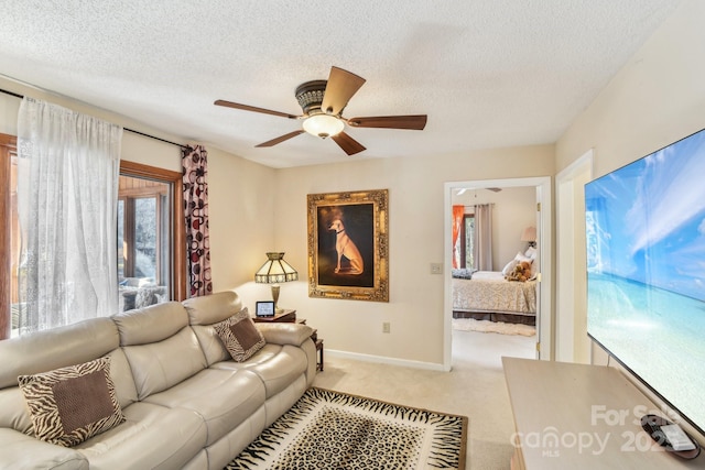 living area with a textured ceiling, ceiling fan, baseboards, and light colored carpet