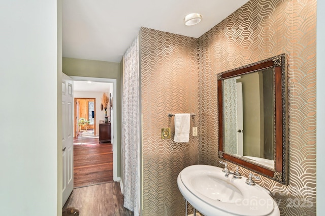 bathroom with wood finished floors, a sink, and wallpapered walls