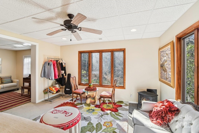 interior space with a paneled ceiling, a ceiling fan, a wood stove, carpet flooring, and baseboards