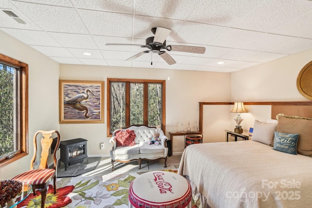 bedroom with baseboards, visible vents, a ceiling fan, a wood stove, and a paneled ceiling