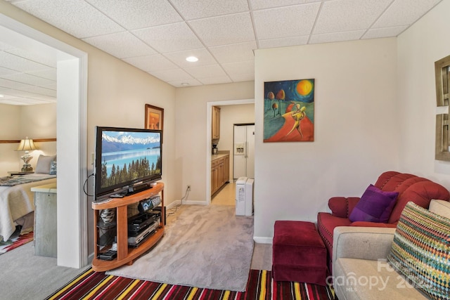 living area featuring light carpet, a paneled ceiling, and baseboards