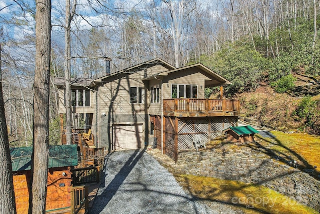 rear view of property featuring a deck, driveway, and an attached garage