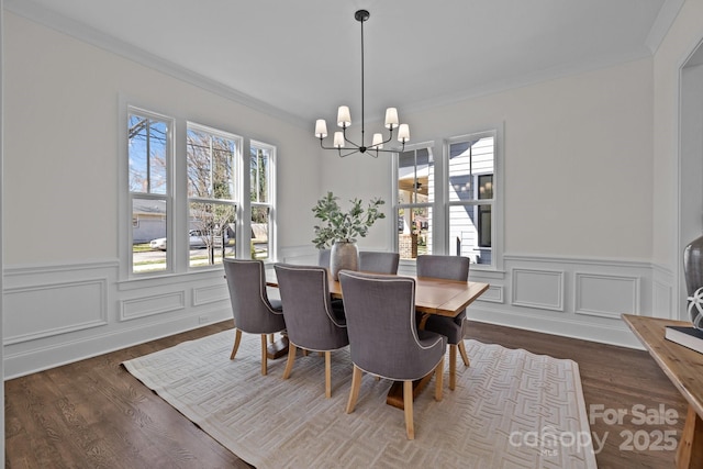 dining space with dark wood-type flooring, crown molding, wainscoting, and a chandelier