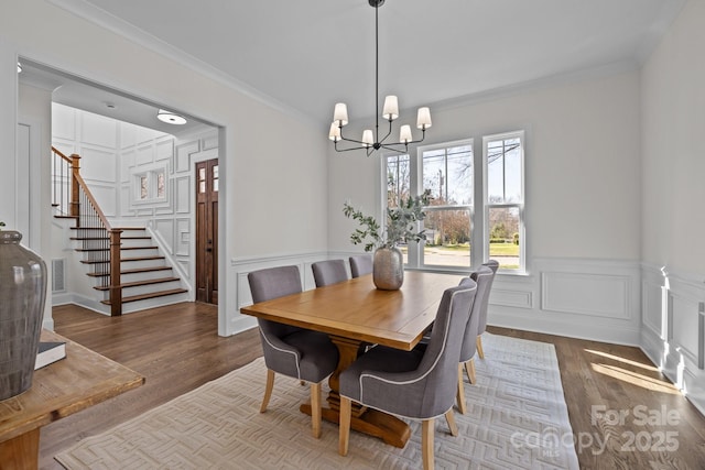 dining area featuring a decorative wall, wood finished floors, stairs, and ornamental molding