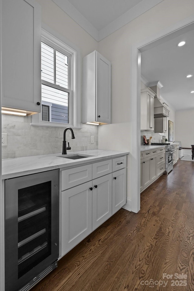 kitchen featuring beverage cooler, high end stove, a sink, crown molding, and wall chimney range hood