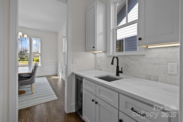 kitchen with beverage cooler, dark wood finished floors, a sink, wainscoting, and backsplash