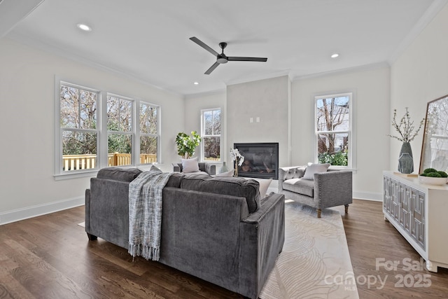 living room featuring dark wood-type flooring, ornamental molding, a glass covered fireplace, recessed lighting, and baseboards