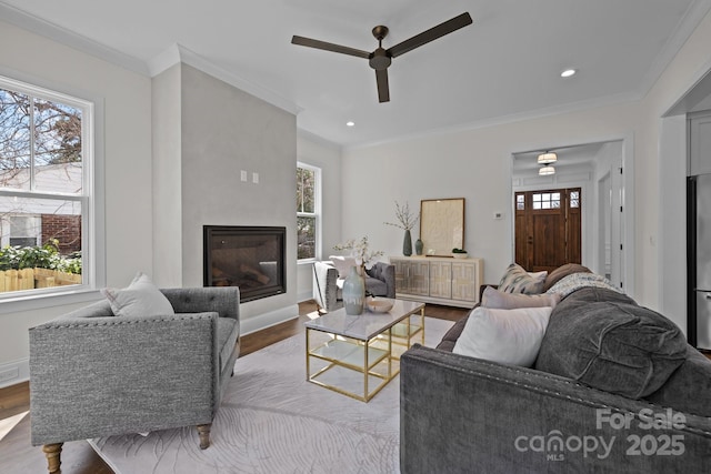 living room with a glass covered fireplace, plenty of natural light, wood finished floors, and crown molding