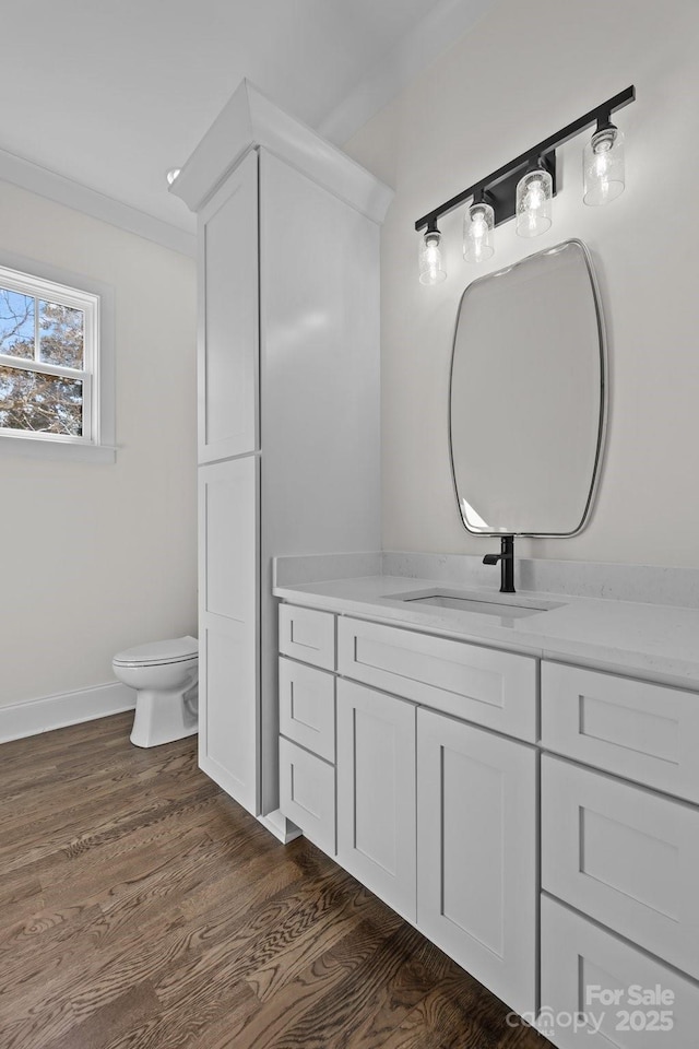 bathroom featuring toilet, vanity, baseboards, and wood finished floors