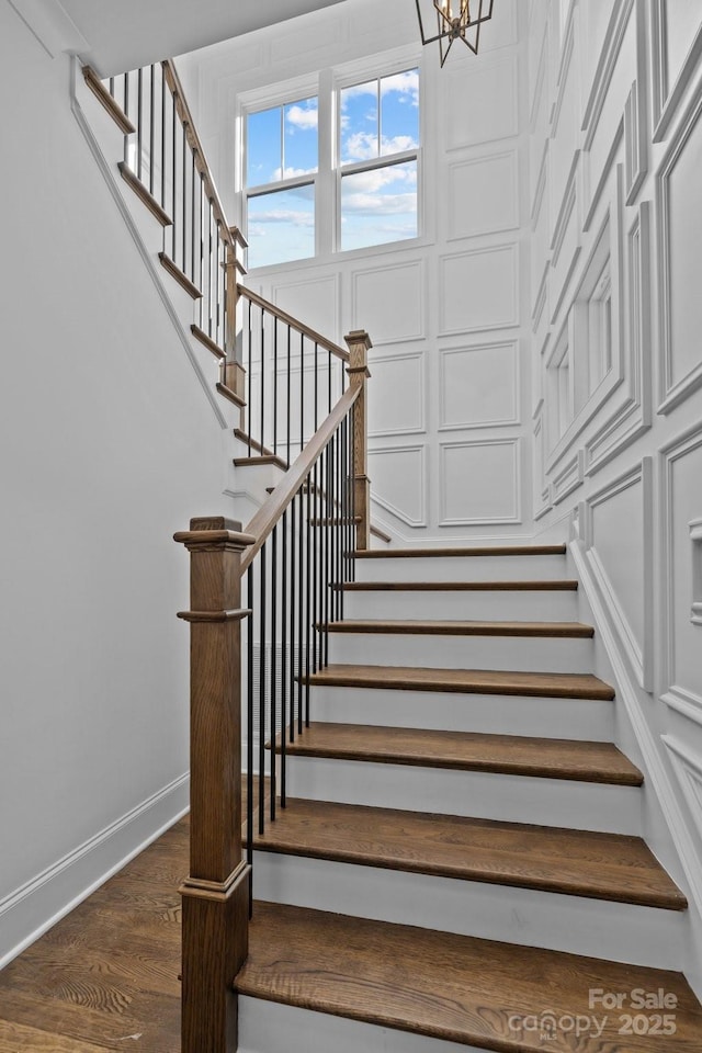 staircase featuring baseboards, an inviting chandelier, and wood finished floors