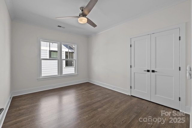 unfurnished bedroom featuring a closet, baseboards, dark wood-style floors, and crown molding