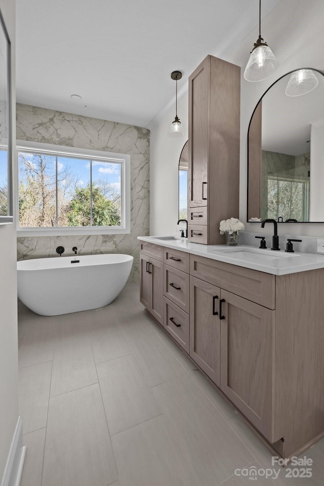 bathroom featuring double vanity, a freestanding bath, tile walls, and a sink