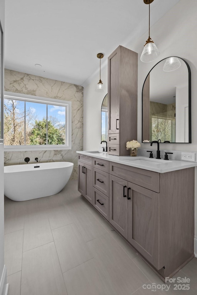 bathroom with a freestanding bath, double vanity, tile walls, and a sink