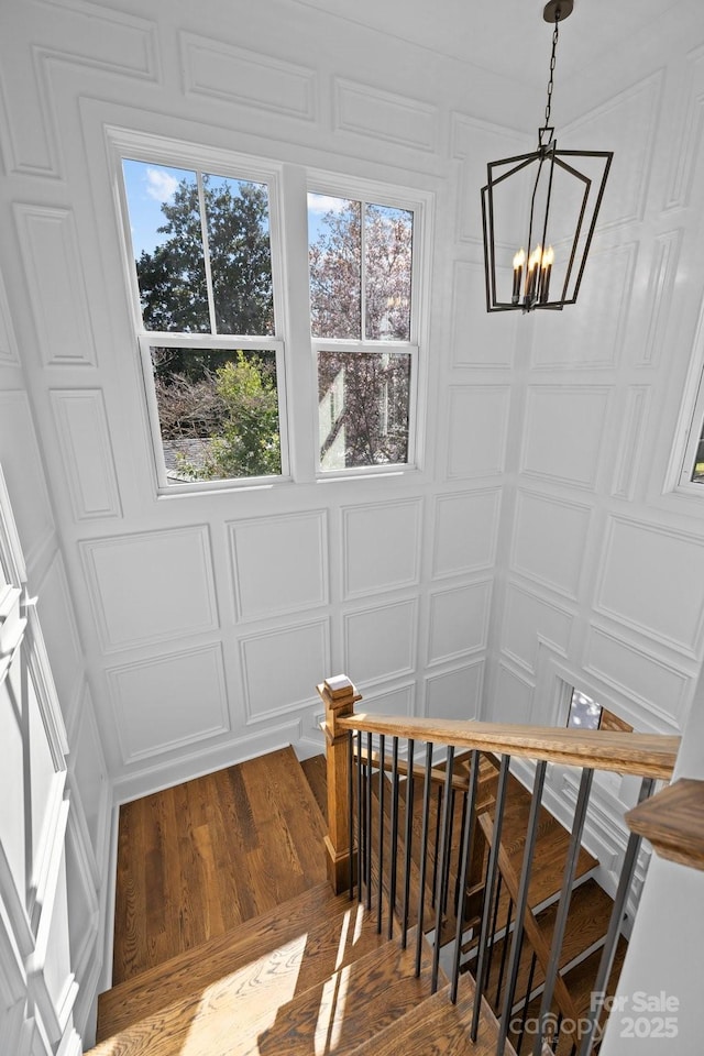 staircase with a decorative wall, wood finished floors, and a chandelier