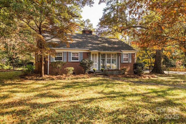 view of front of property featuring brick siding, a chimney, a front lawn, and fence