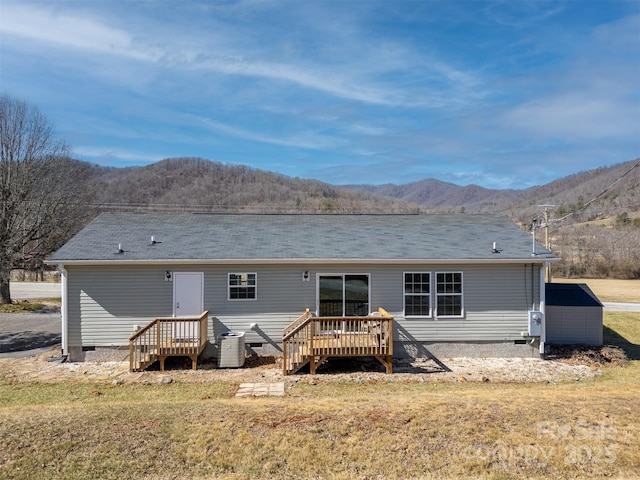 rear view of property featuring cooling unit, a deck with mountain view, and a lawn