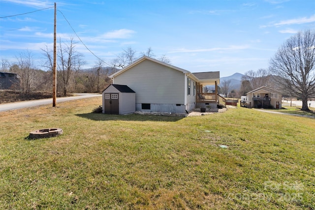 view of side of property featuring a shed, a mountain view, a fire pit, and a lawn