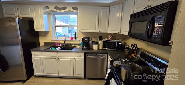 kitchen with white cabinets, dark countertops, stainless steel appliances, light wood-style floors, and a sink