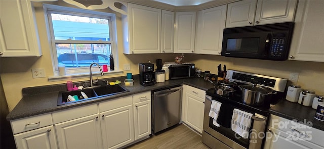 kitchen featuring light wood finished floors, dark countertops, appliances with stainless steel finishes, white cabinets, and a sink