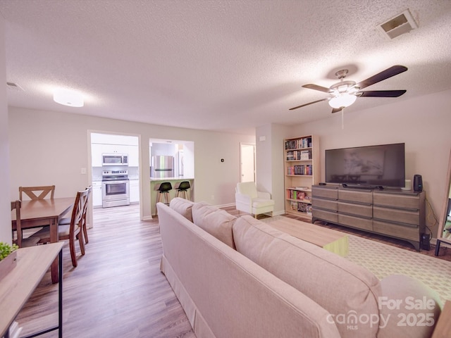 living room with ceiling fan, light hardwood / wood-style flooring, and a textured ceiling