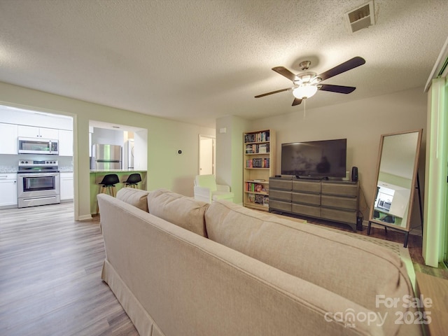 living room with ceiling fan, light hardwood / wood-style floors, and a textured ceiling