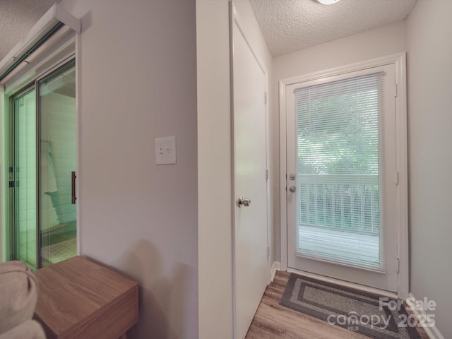 doorway with a healthy amount of sunlight, a textured ceiling, and light hardwood / wood-style flooring