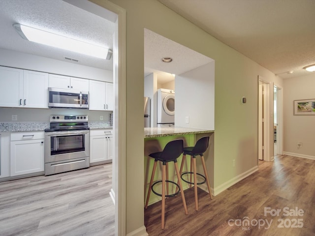 kitchen with washer / clothes dryer, white cabinetry, light hardwood / wood-style floors, light stone counters, and stainless steel appliances